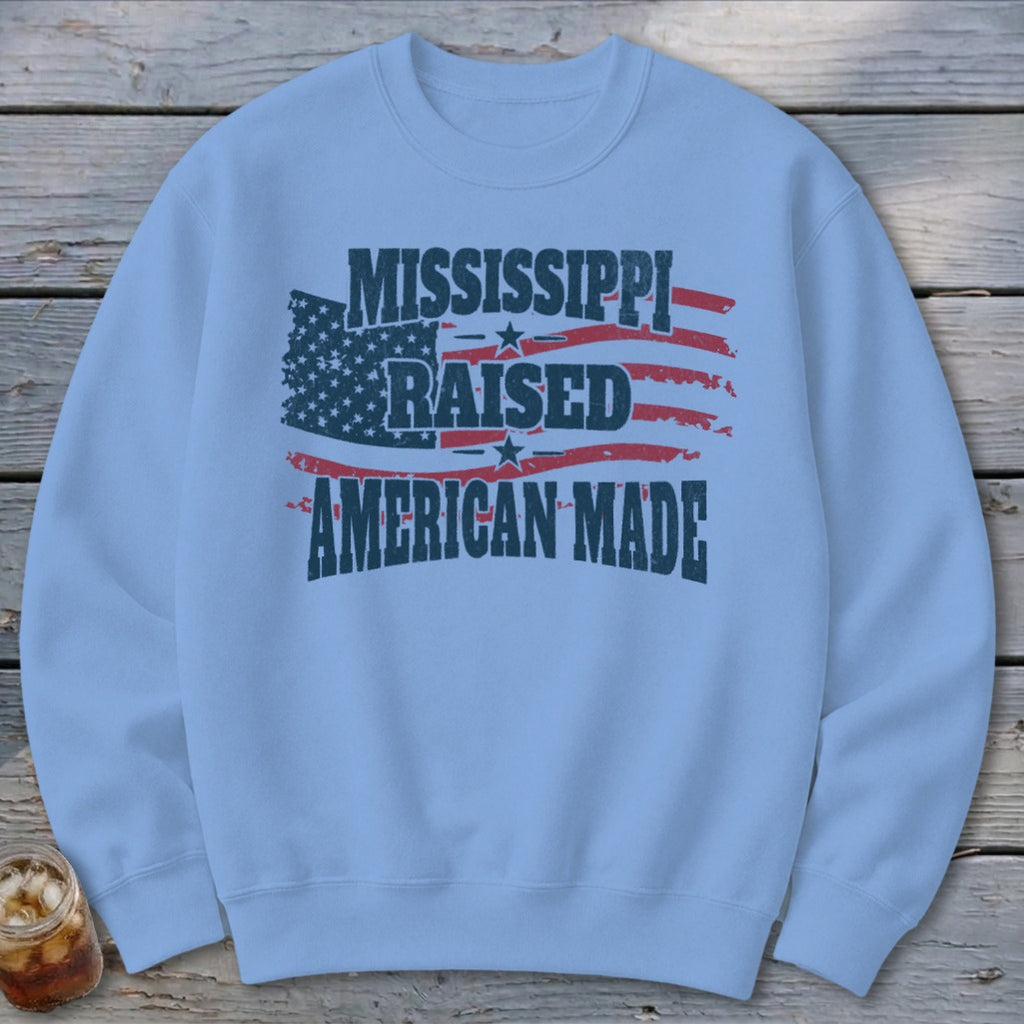 Light blue crewneck sweatshirt featuring a distressed American flag and text that reads Mississippi Raised American Made.