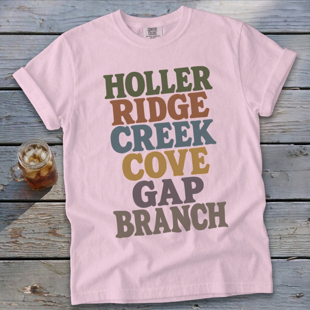 A pink t-shirt featuring stacked multicolored text reading HOLLER RIDGE CREEK COVE GAP BRANCH.