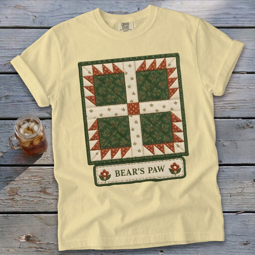 Yellow t-shirt with a quilt design and "Bear's Paw" text, next to a glass of iced tea.
