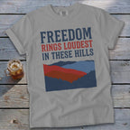 Grey t-shirt with "FREEDOM RINGS LOUDEST IN THESE HILLS" text and mountain graphic.