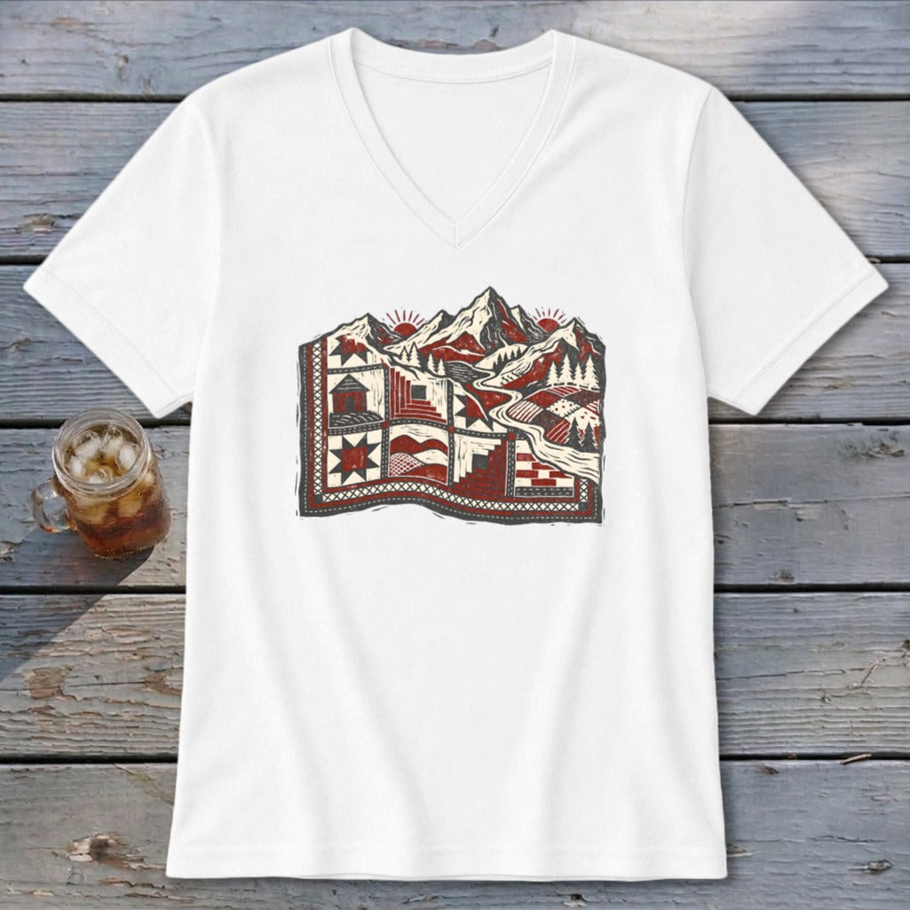 A white V-neck t-shirt featuring a vintage red, black, and white mountain quilt graphic laid on weathered wood.