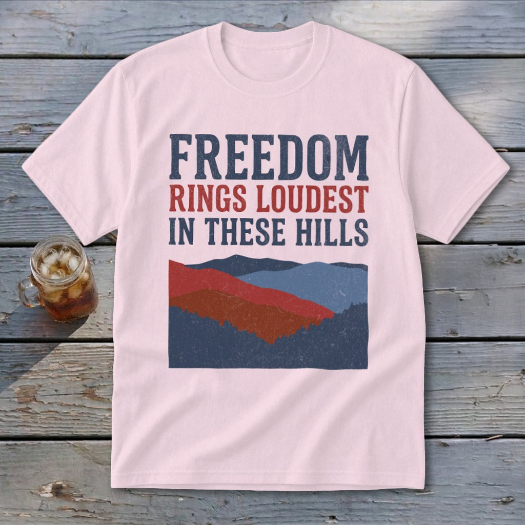 Light pink t-shirt featuring distressed blue and red text reading Freedom Rings Loudest in These Hills above layered mountain graphics.