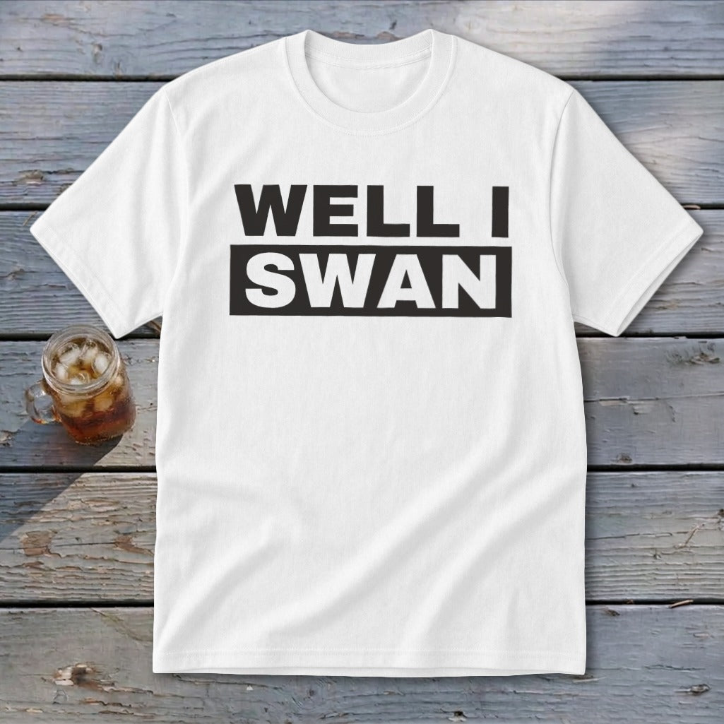 White crewneck t-shirt with black text that reads WELL I SWAN on a wooden background.