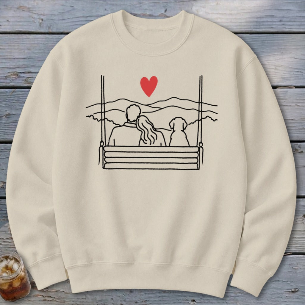 Cream sweatshirt with line drawing of couple and dog on swing, red heart above.