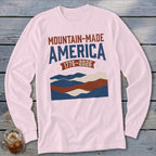 A light pink long-sleeve shirt featuring a graphic with the text Mountain-Made America 1776-2026 over abstract mountains.