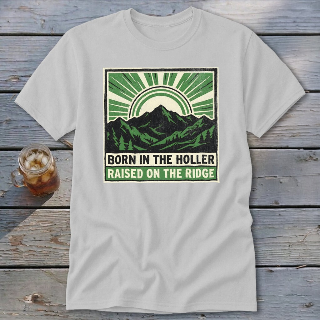 Light gray t-shirt with a green graphic of mountains, sun rays, and text that reads Born in the Holler, Raised on the Ridge.