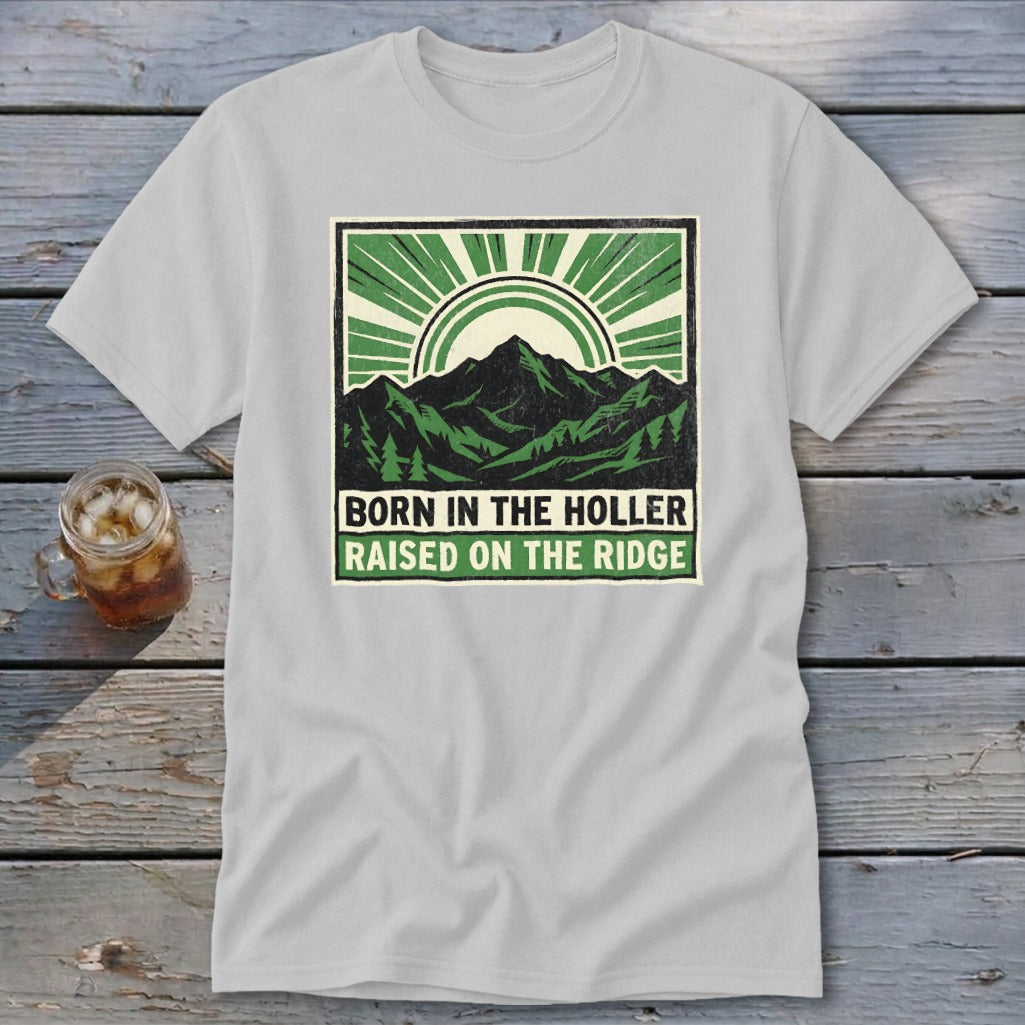 Light gray t-shirt with a green graphic of mountains, sun rays, and text that reads Born in the Holler, Raised on the Ridge.