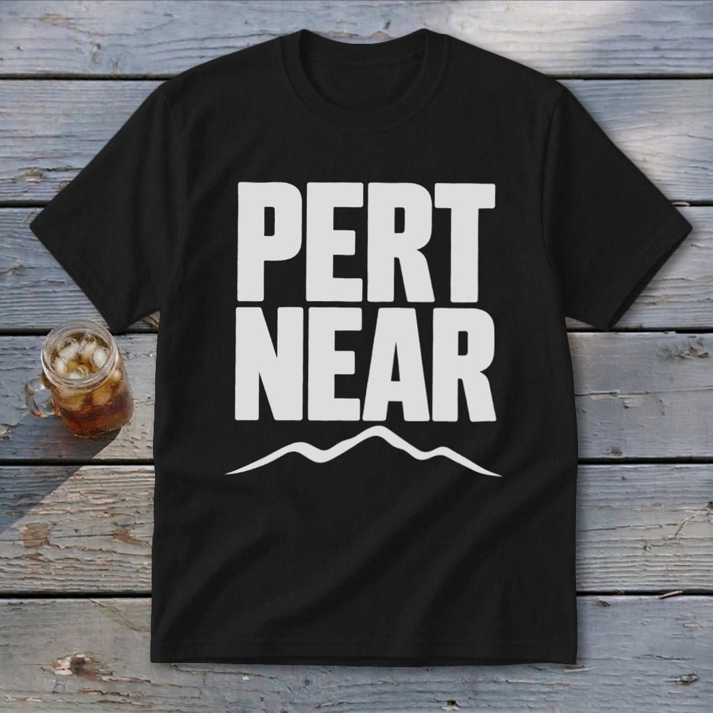 Black t-shirt featuring the white text PERT NEAR above a mountain range graphic, laid on wood planks.
