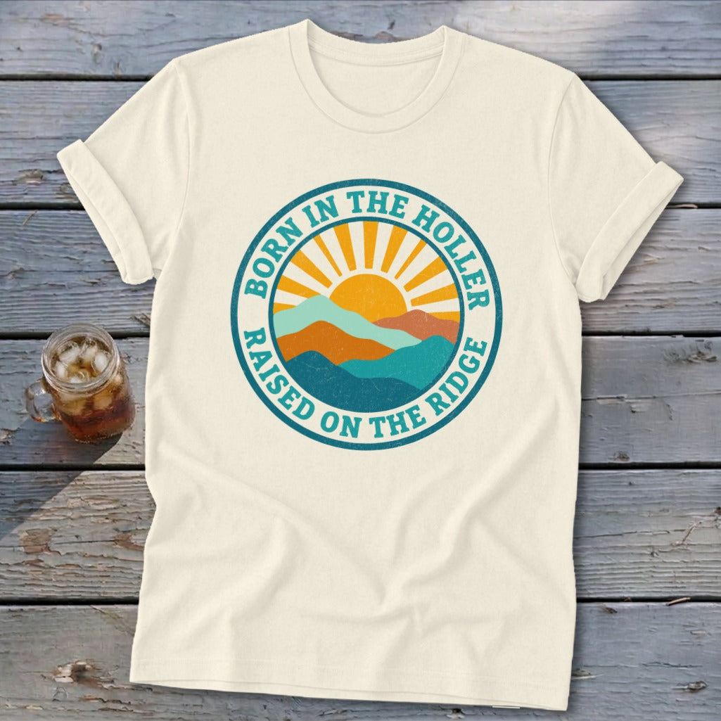 Cream t-shirt with a round graphic of mountains and a sun, plus text reading Born in the Holler Raised on the Ridge.