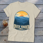 Beige t-shirt featuring a retro graphic of mountains, pine trees, a sunset, and the text Over Yonder.