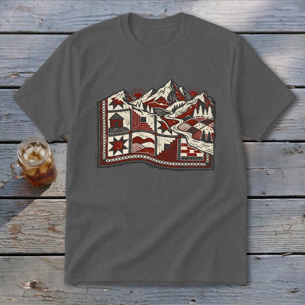 Charcoal t-shirt featuring a stylized graphic of mountains, trees, and cabins resembling a quilt on a wooden surface.