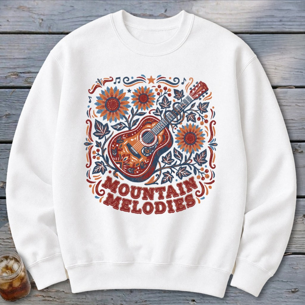A white crewneck sweatshirt featuring a colorful folk-art design of a guitar, sunflowers, and the text MOUNTAIN MELODIES.