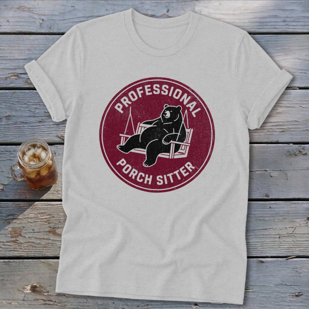 A light gray t-shirt featuring a circular maroon graphic of a bear lounging in a porch swing, surrounded by the text Professional Porch Sitter.