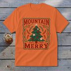 An orange crew neck t-shirt featuring a green Christmas tree graphic and the text Mountain Merry.
