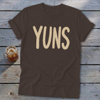Brown t-shirt with beige text "YUNS" and a glass of iced tea.