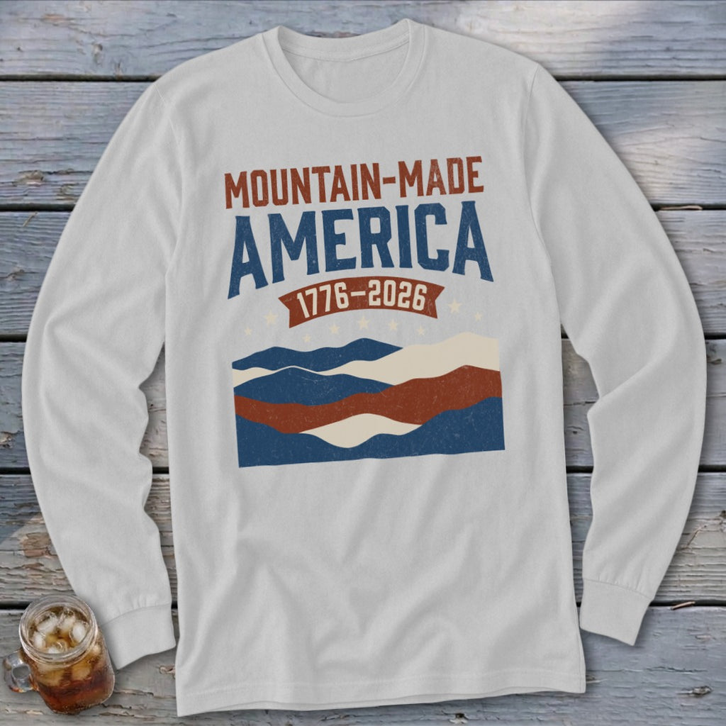Light gray long-sleeve t-shirt with a red, white, and blue mountain graphic and the text MOUNTAIN-MADE AMERICA 1776-2026.