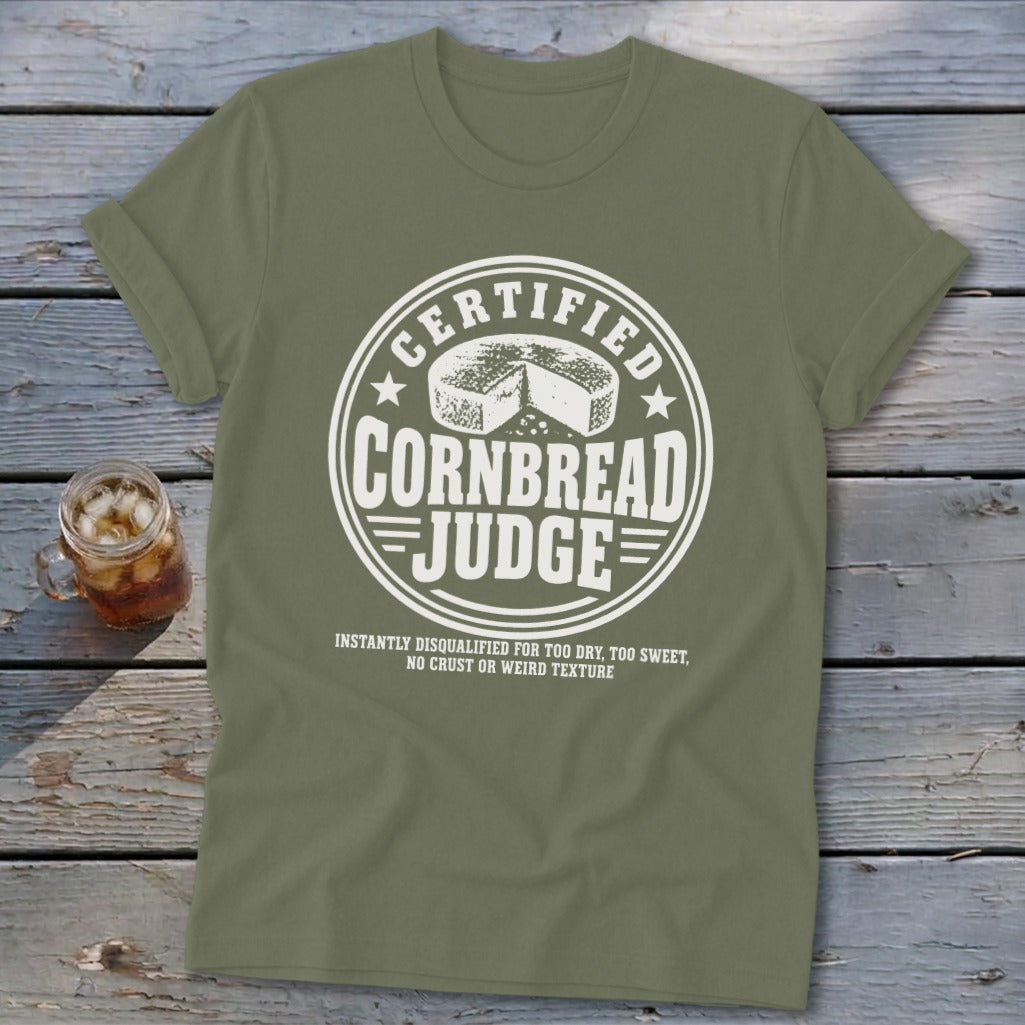 Olive green t-shirt featuring a circular white graphic with a cornbread illustration and text reading Certified Cornbread Judge.