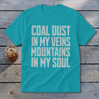 A teal t-shirt featuring the distressed white text COAL DUST IN MY VEINS MOUNTAINS IN MY SOUL.
