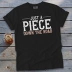 Black t-shirt with white text that reads "JUST A PIECE DOWN THE ROAD."