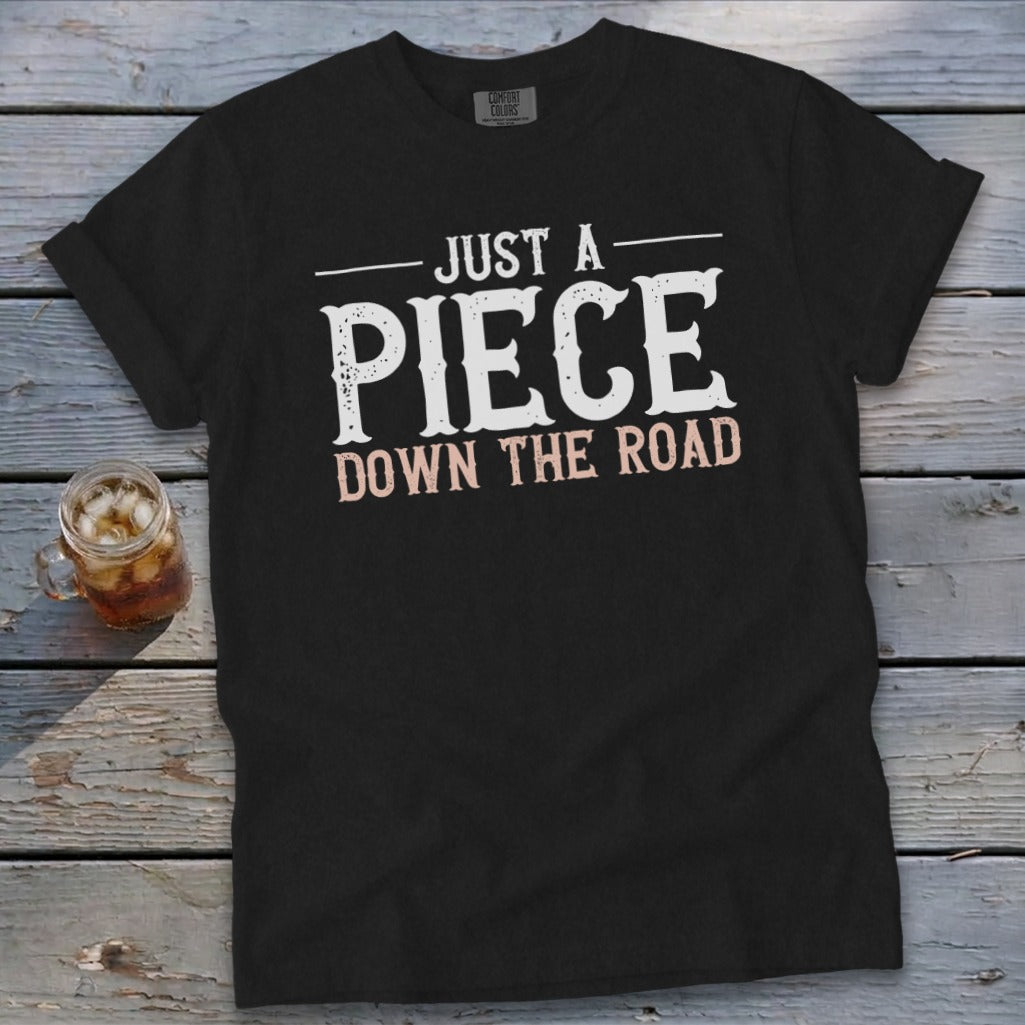 Black t-shirt with white text that reads "JUST A PIECE DOWN THE ROAD."