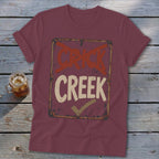 Maroon t-shirt with a sign graphic reading "CRICK" crossed out and "CREEK" with a checkmark.