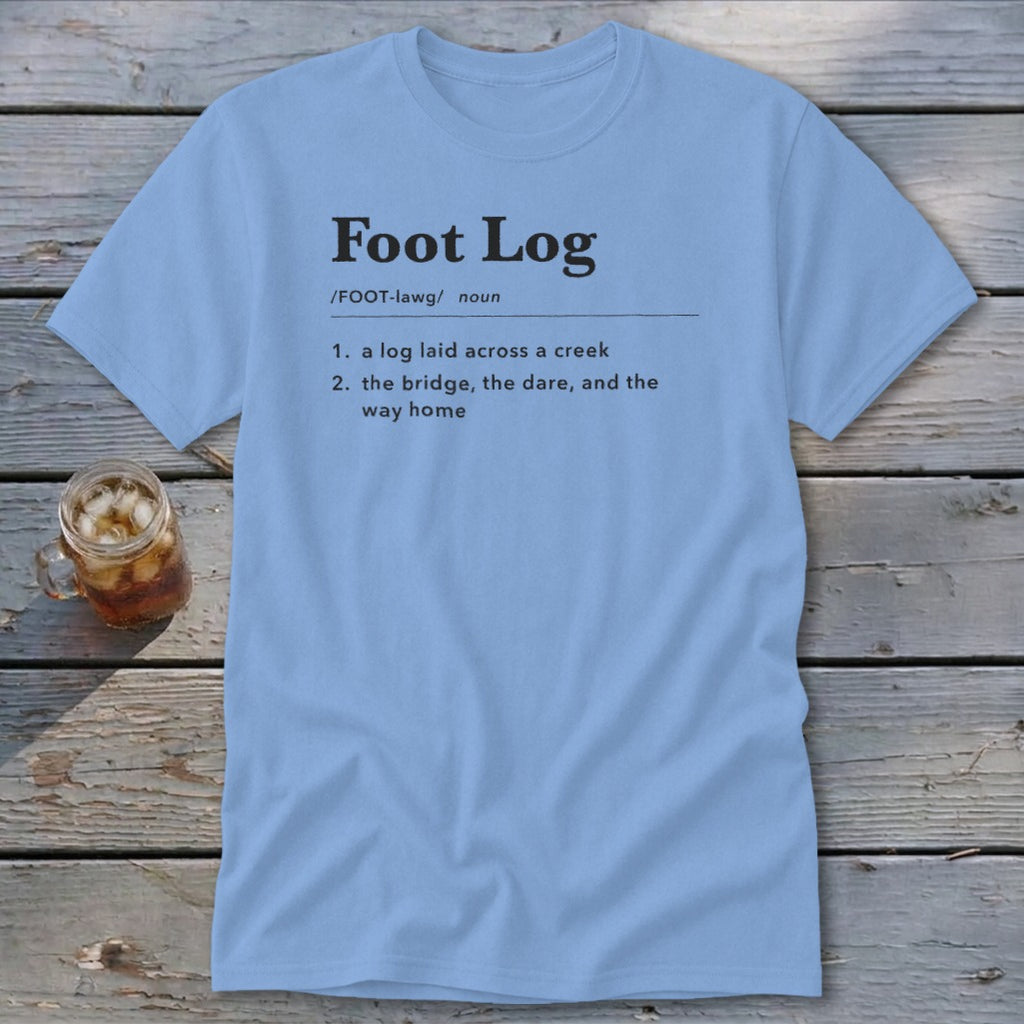 Light blue t-shirt featuring dictionary-style text defining Foot Log laid across a wooden surface.