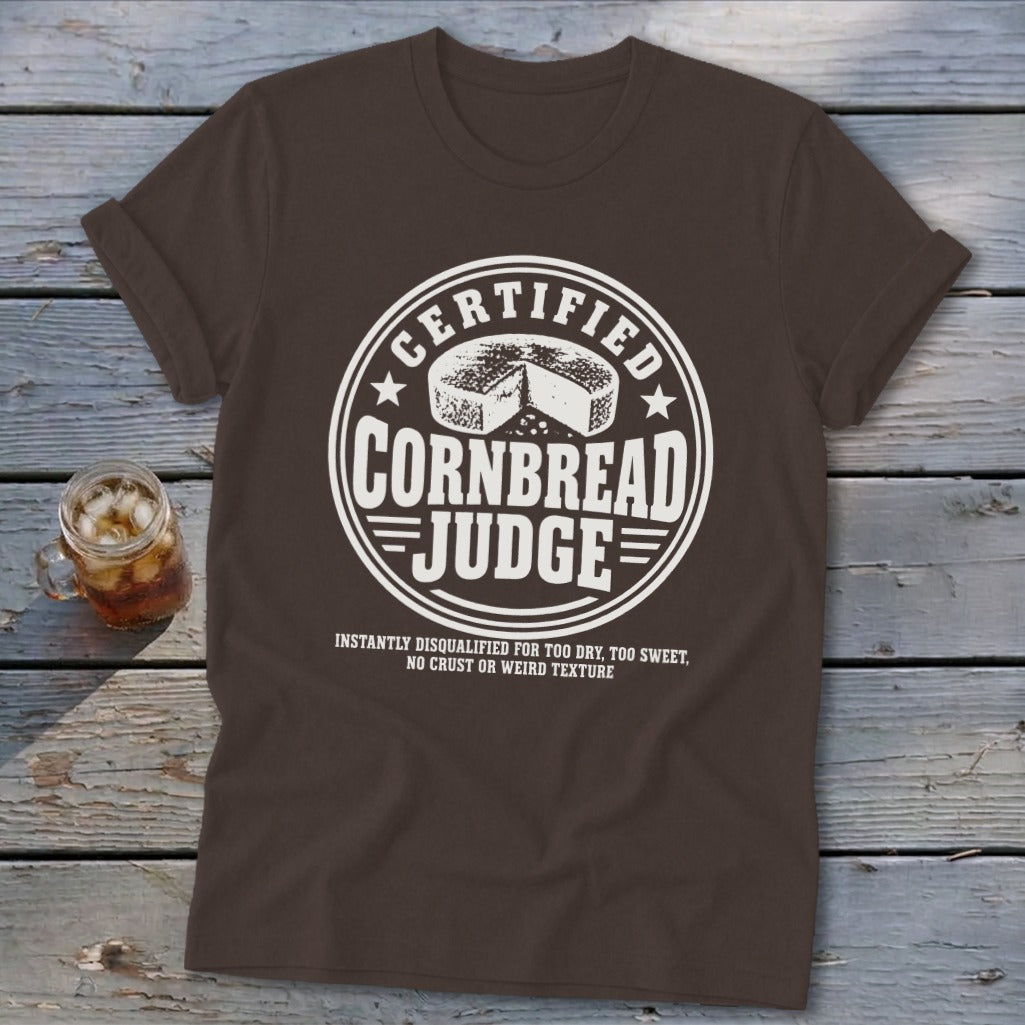 Brown short-sleeve t-shirt featuring a white graphic emblem reading Certified Cornbread Judge and a small drink beside it.