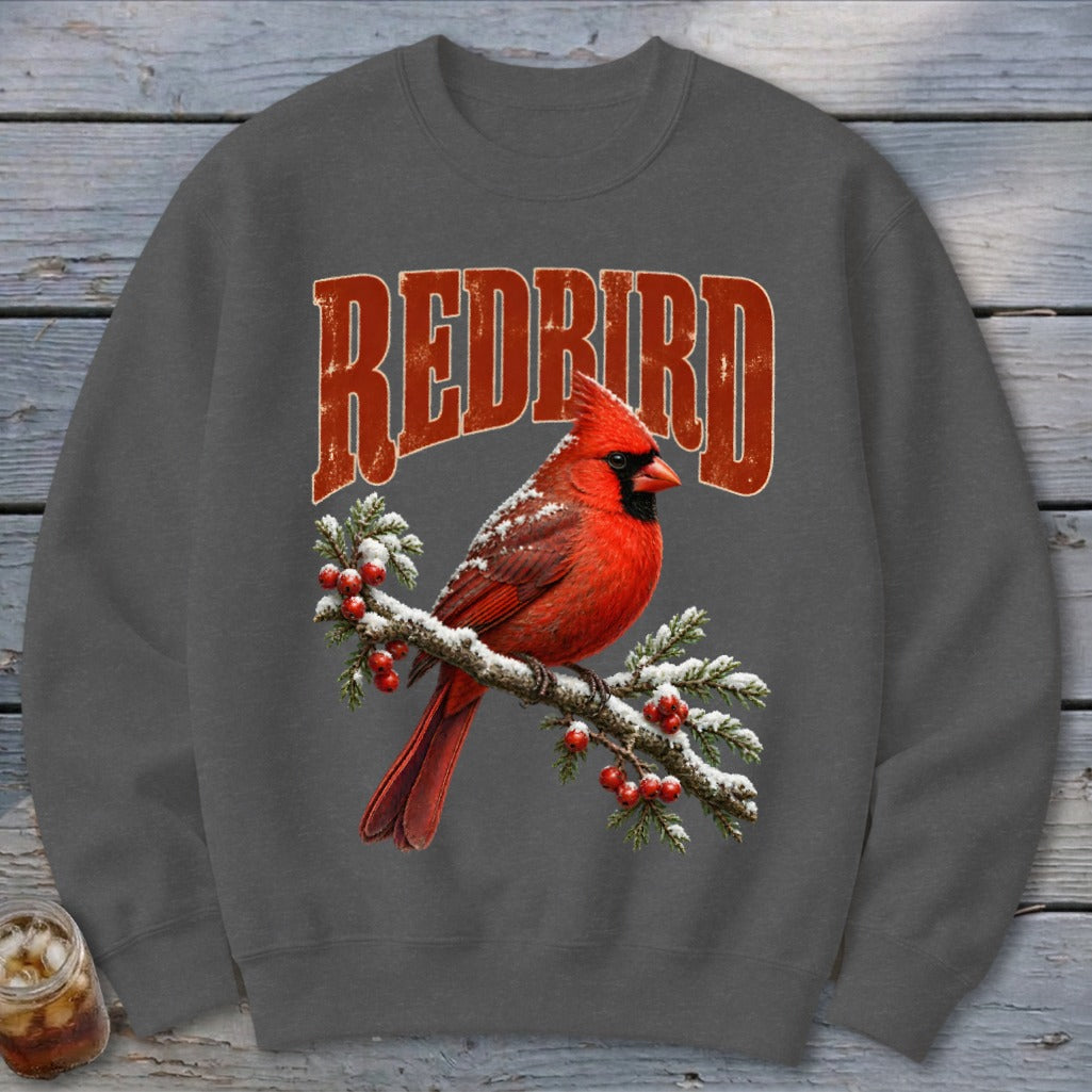 A dark gray crewneck sweatshirt featuring a graphic of a red cardinal on a snow-covered branch beneath the text REDBIRD.