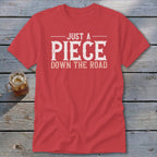 Red t-shirt with white distressed text reading "JUST A PIECE DOWN THE ROAD".