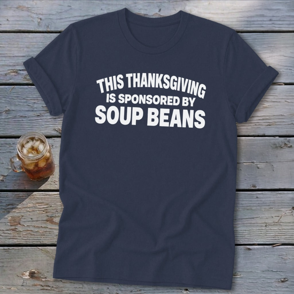 Navy blue t-shirt featuring the white text THIS THANKSGIVING IS SPONSORED BY SOUP BEANS on a wooden surface.