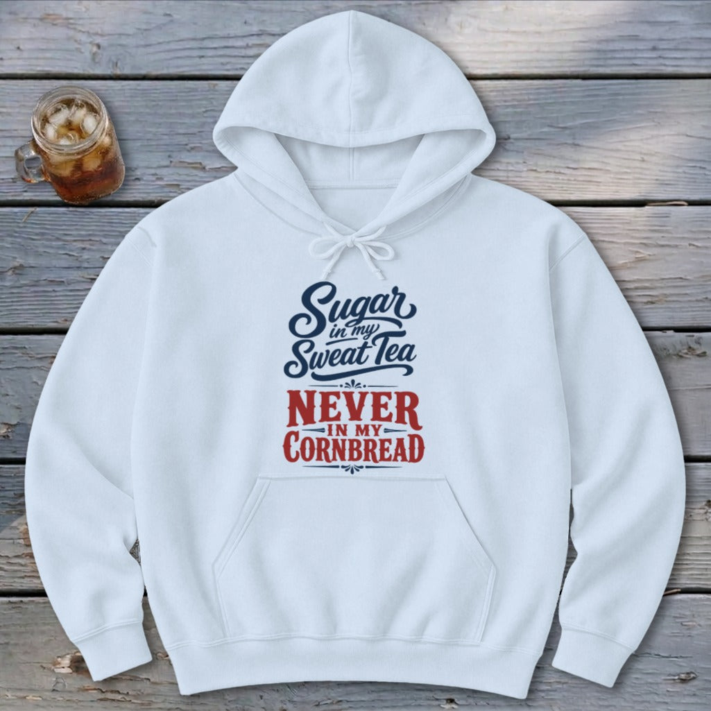 A white hooded sweatshirt featuring blue and red text reading Sugar in my Sweet Tea Never in my Cornbread on a wooden background.