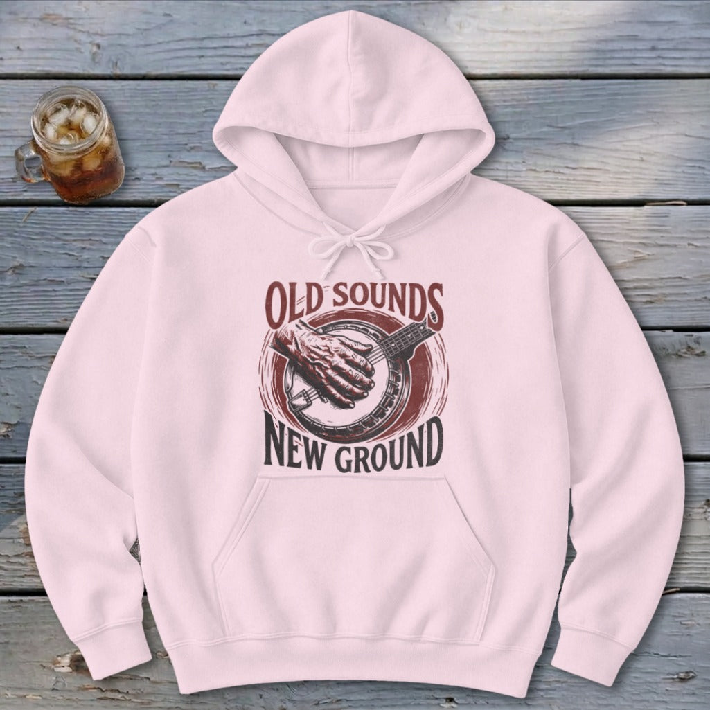 Light pink hooded sweatshirt featuring a graphic of a hand playing a banjo and text that reads Old Sounds New Ground.