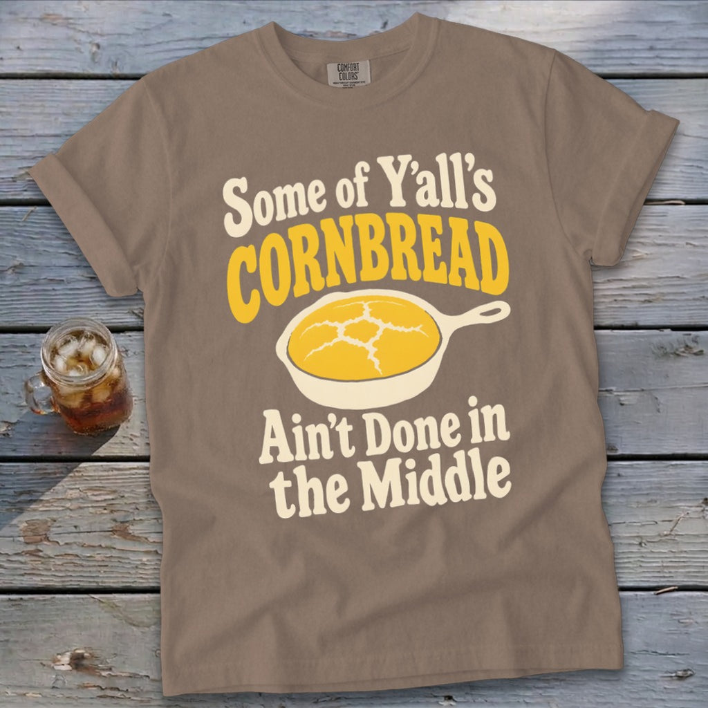 Brown t-shirt featuring the text "Some of Y'all's Cornbread Ain't Done in the Middle" and a cast-iron skillet graphic.