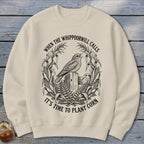 Beige crewneck sweatshirt featuring a black graphic of a bird on a wooden post surrounded by cornstalks and text.