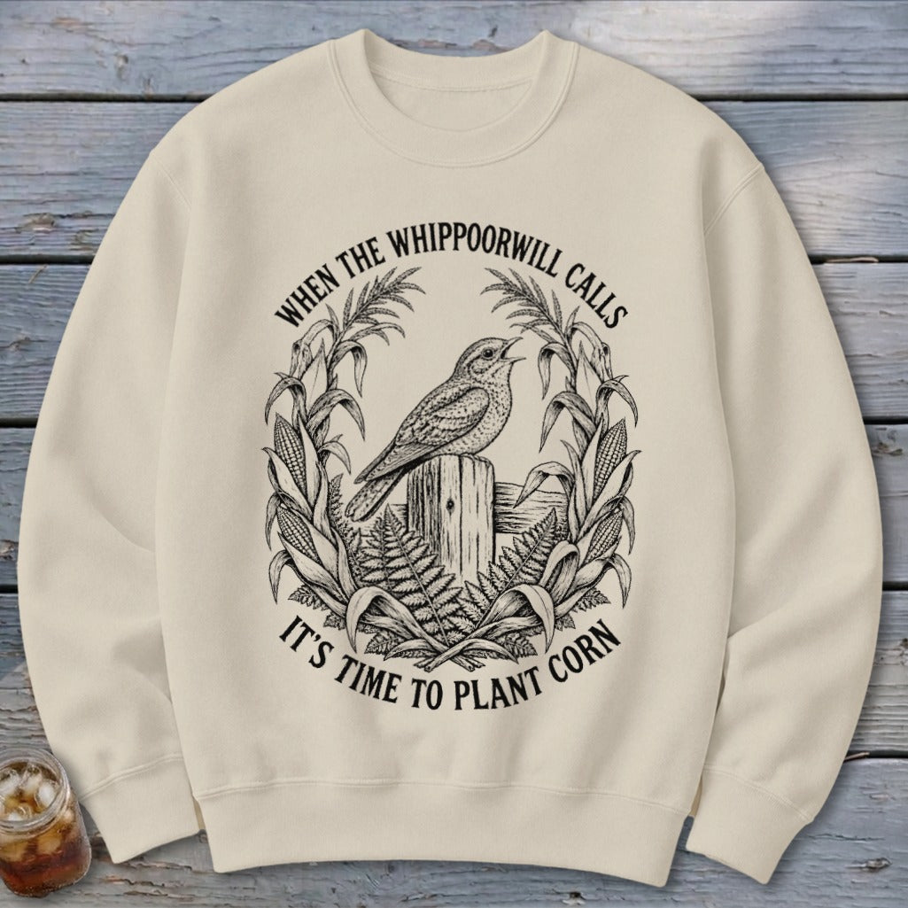 Beige crewneck sweatshirt featuring a black graphic of a bird on a wooden post surrounded by cornstalks and text.