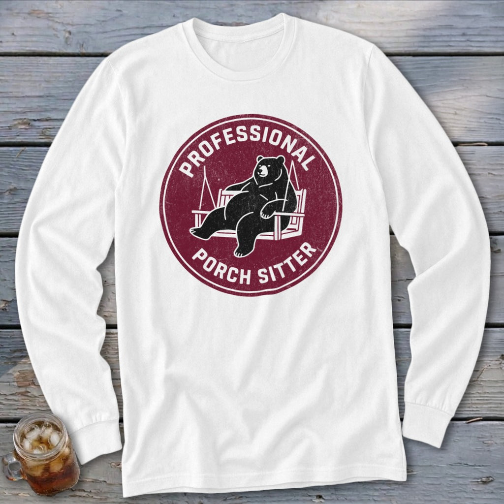 A white long-sleeved t-shirt features a circular maroon graphic of a bear lounging on a swing with text.