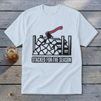 White t-shirt graphic of stacked firewood with axe and text "STACKED FOR THE SEASON".