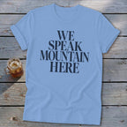 Light blue t-shirt with "WE SPEAK MOUNTAIN HERE" text and a drink.
