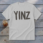 White t-shirt with dark gray "YINZ" text, and a glass of iced beverage.