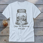 A white t-shirt featuring a mason jar illustration filled with a mountain landscape and text reading Carry The Mountains With You.