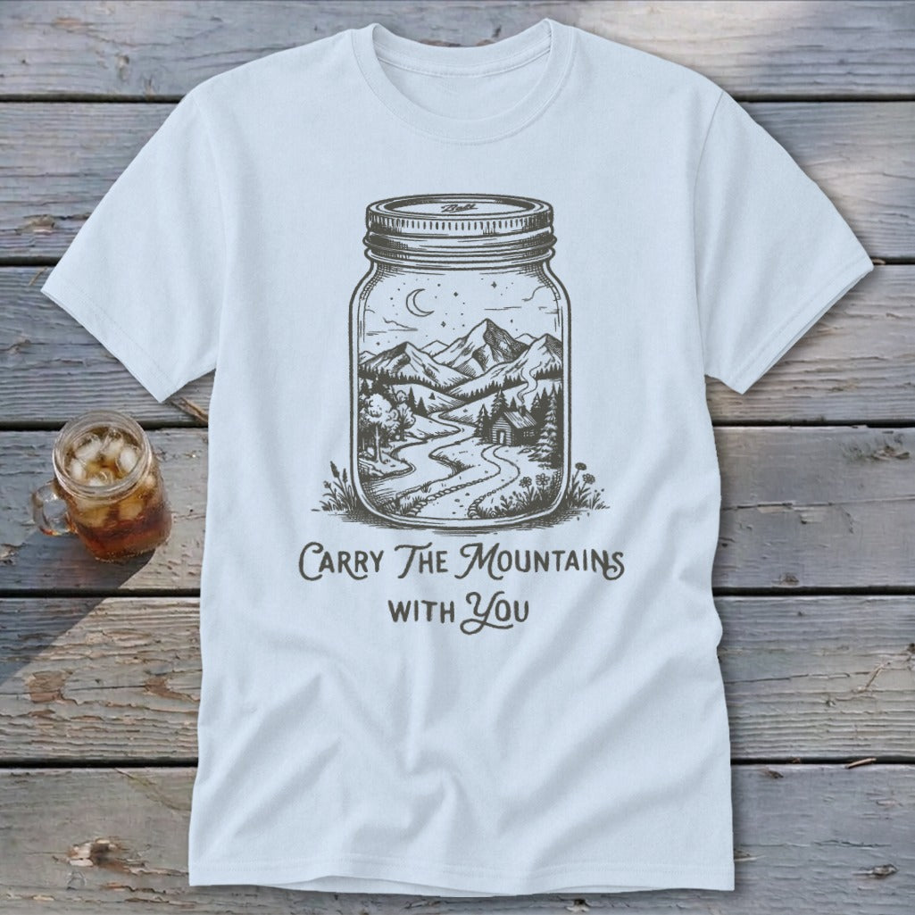 A white t-shirt featuring a mason jar illustration filled with a mountain landscape and text reading Carry The Mountains With You.