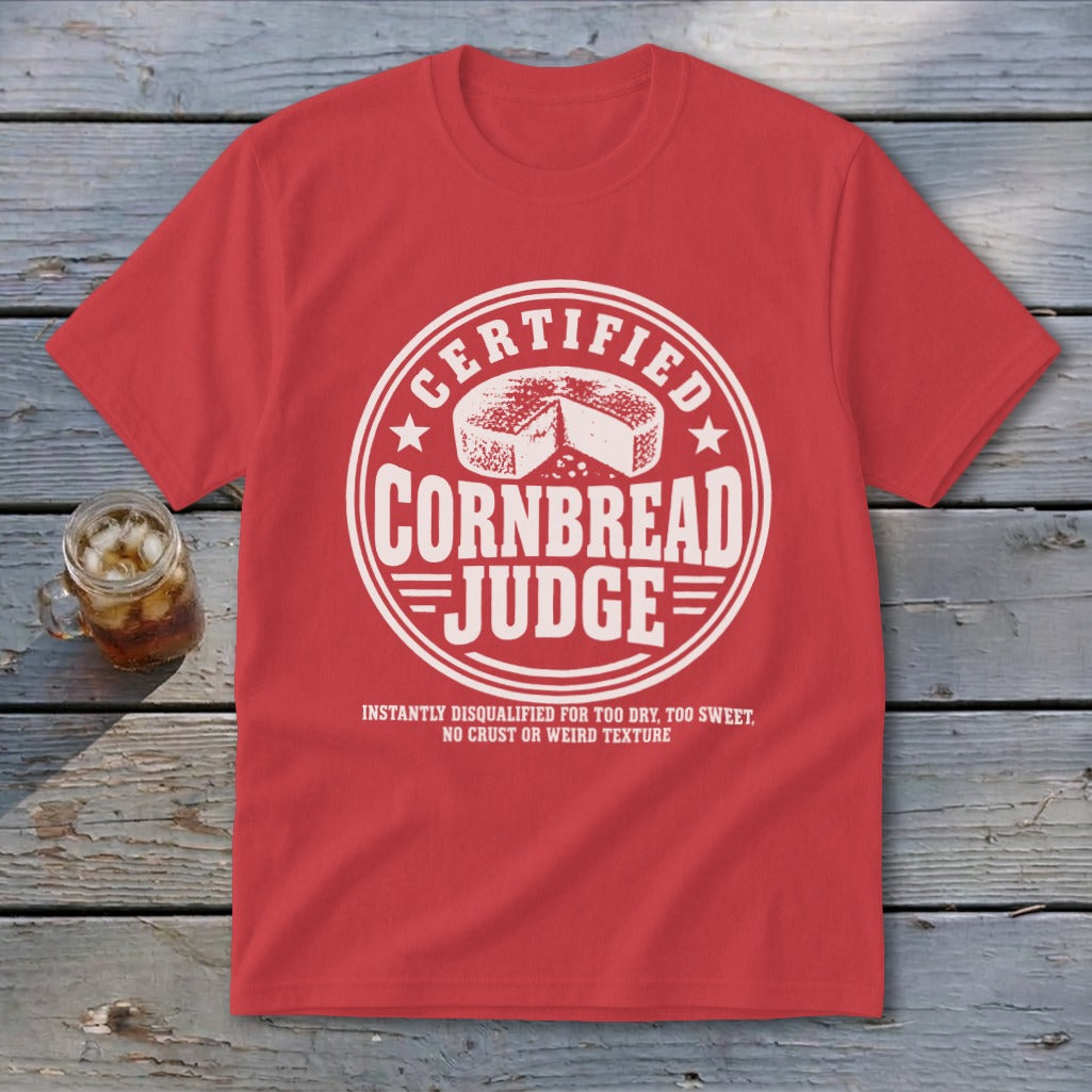 A red short-sleeved t-shirt with a white graphic featuring a cornbread illustration and text reading Certified Cornbread Judge.