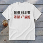 White t-shirt with "THESE HOLLERS KNOW MY NAME" printed in black and red text.