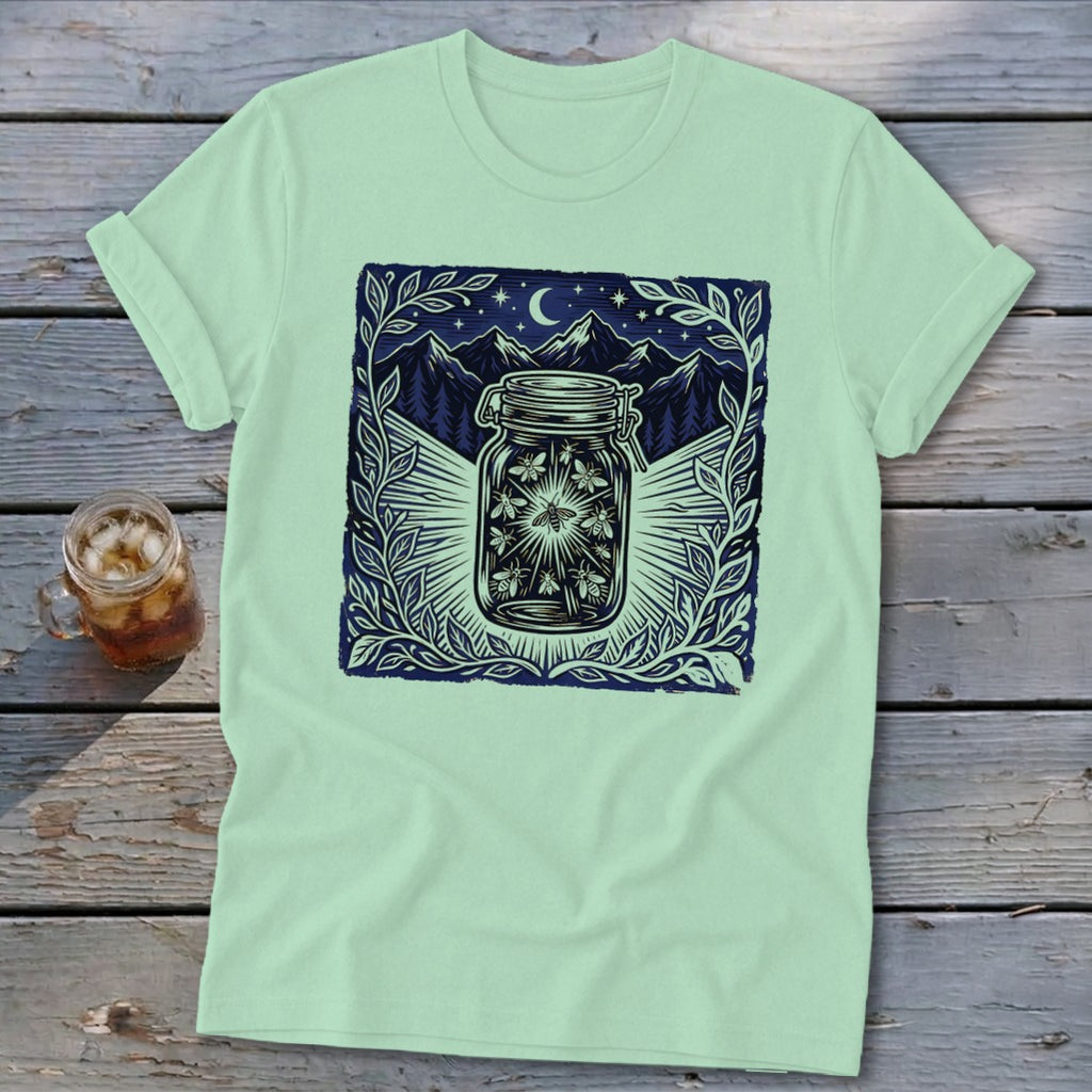 Light green t-shirt with a dark blue graphic of fireflies in a jar under a moonlit mountain sky.