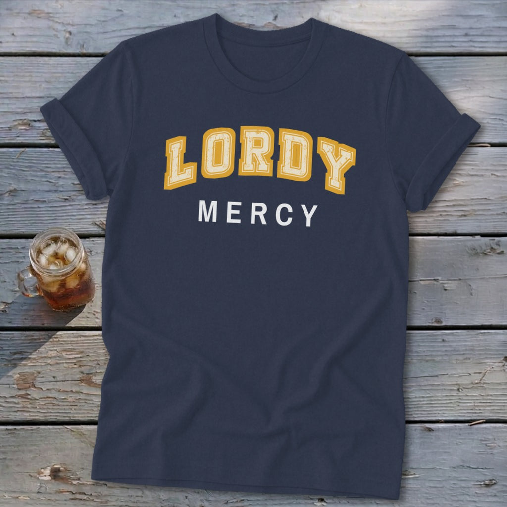 Navy t-shirt with yellow "LORDY" and white "MERCY" text on wooden background.