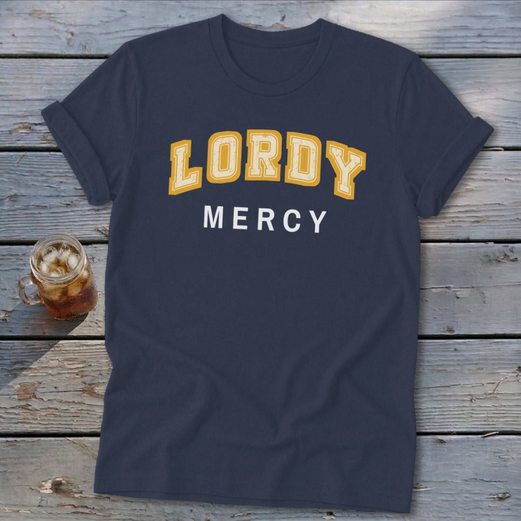 Navy t-shirt with yellow "LORDY" and white "MERCY" text on wooden background.