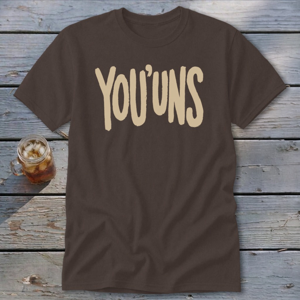 Brown t-shirt with "YOU'UNS" text in beige, next to a glass of iced tea.