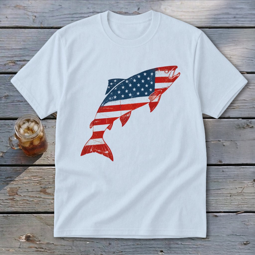 A white t-shirt featuring a leaping fish graphic filled with the American flag pattern rests on a wooden surface.