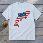 A white t-shirt featuring a leaping fish graphic filled with the American flag pattern rests on a wooden surface.