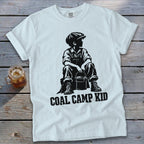 White t-shirt with black graphic of a boy sitting with a bucket and "COAL CAMP KID" text.